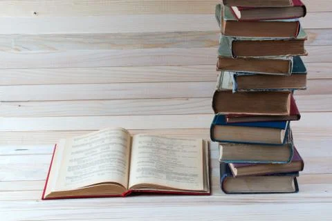 Open book, stack of hardback books on wooden table. Stock Photos