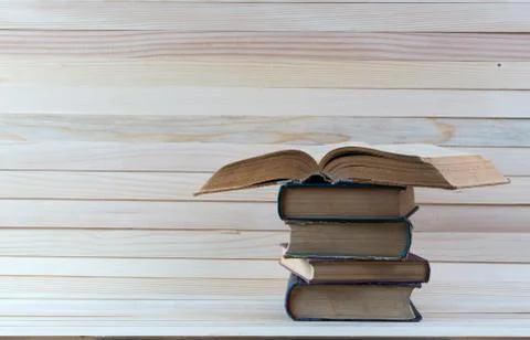 Open book, stack of hardback books on wooden table. Stock Photos