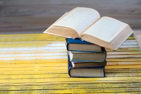 Open book, stack of hardback books on wooden table. Stock Photos