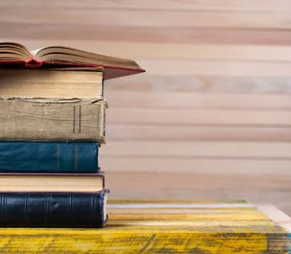 Open book, stack of hardback books on wooden table. Stock Photos