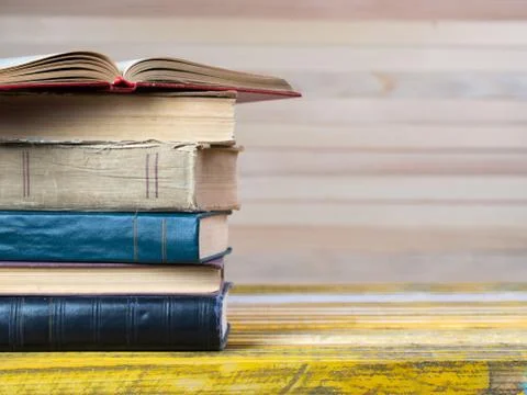 Open book, stack of hardback books on wooden table. Stock Photos