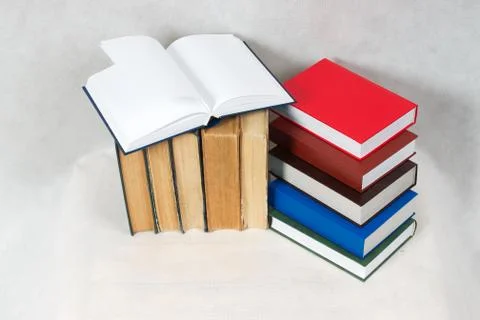 Open book, stack of hardback books on table Stock Photos