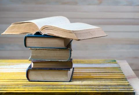 Open book, stack of hardback books on wooden table. Stock Photos