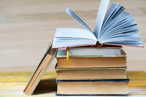 Open book, stack of hardback books on wooden table. Stock Photos