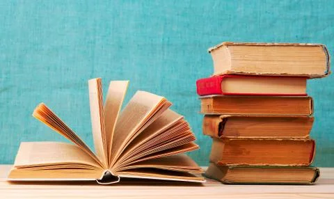 Open book, stack of hardback books on wooden table. Stock Photos