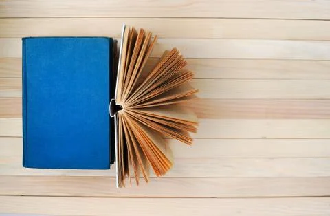 Open book, stack of hardback books on wooden table. Stock Photos
