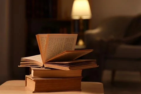 Open book on stack of old books with warm lamp light in cozy home library set Stock Photos