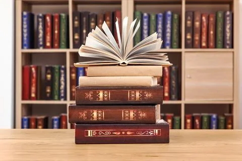 Open book on stack of old books with bookshelf background, education and know Stock Photos