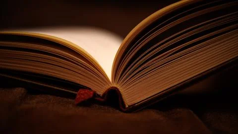 Open book with warm light on pages dark background close-up Stock Photos