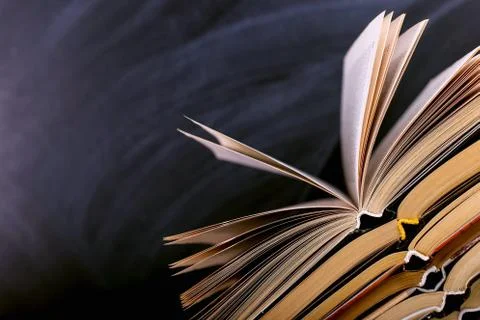 Open books are a stack on the desk, against the background of a chalk board.  Stock Photos
