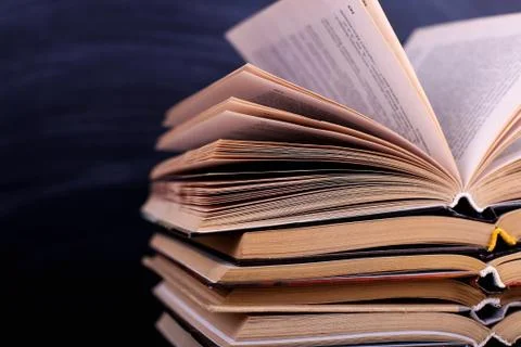 Open books are a stack on the desk, against the background of a chalk board.  Stock Photos