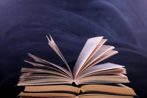 Open books are a stack on the desk, against the background of a chalk board.  Stock Photos