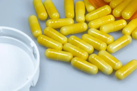 An open bottle of yellow capsules laying across a white table Stock Photos