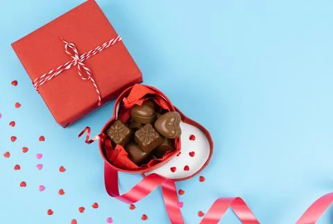 Open box in the shape of a heart full of chocolates on a blue background. Stock Photos