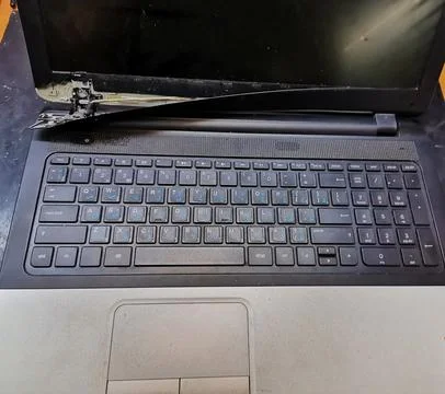 An open, broken laptop computer showing severe damage to the left hinge and a Stock Photos