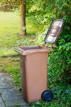 Open brown plastic bio-waste bin for composting standing in a green backyard  Fotos Stock