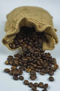 Open burlap sack spilling roasted coffee beans on white surface Stock Photos