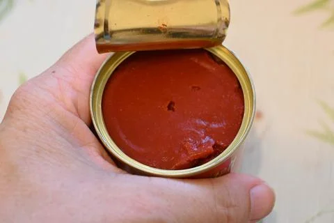 Open can of tomato paste held by hand Stock Photos