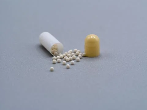 Open capsule with white pellets on gray background Stock Photos