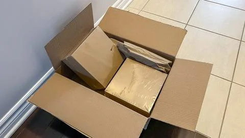 Open cardboard box containing several packages wrapped in brown paper and bubble Stock Photos