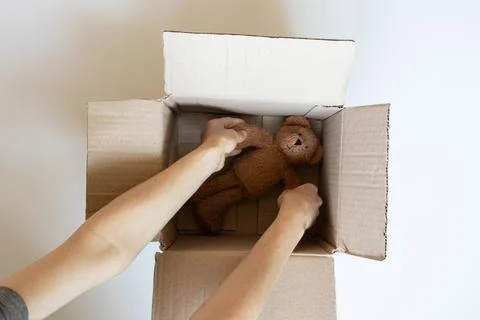 An open cardboard box with a teddy bear and wrapping paper, and a girl's ha.. Stock Photos