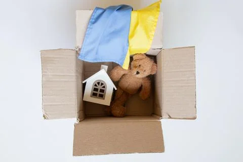 An open cardboard box with a teddy bear, a toy house, and the Ukrainian flag, Stock Photos