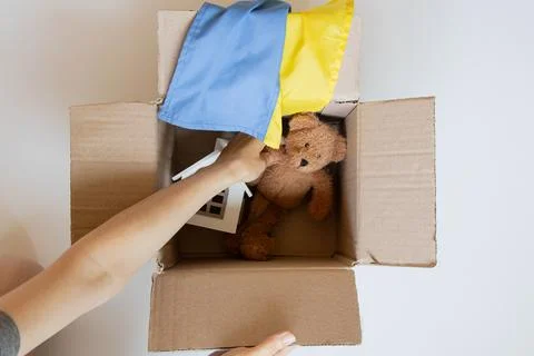 An open cardboard box with a teddy bear, a toy house, and the Ukrainian flag, Stock Photos