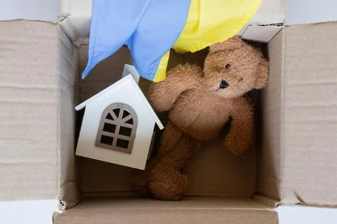 An open cardboard box with a teddy bear, a toy house, and the Ukrainian flag, Stock Photos