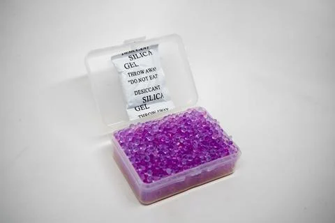 An open clear plastic container filled with purple silica gel beads and a w.. Stock-Fotos
