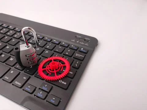 An open combination padlock and a red plastic gear rest on top of a black c.. 스톡 사진