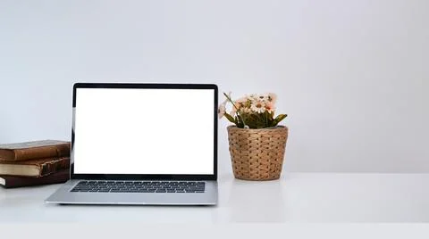 Open computer laptop with empty screen, books and flowers pot on white desk. Stock Photos