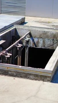 An open concrete underground utility hatch or service pit featuring metal sup Stock Photos