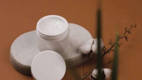 Open cosmetic jar displaying rich cream texture beside lid on stone pedestal Stock Footage 342377984