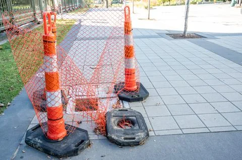 Open cover on a sidewalk access panel with hazard cones and fencing. Foto stock