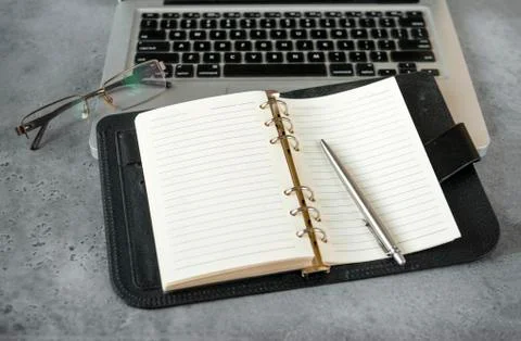 Open diary with blank sheets, laptop, pen, glasses on a gray Stock Photos