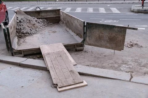 Open dumpster partially filled with construction waste is placed on a road .. Stock Photos