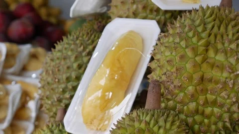 Open durian fruit placed beside whole spiky durians with other fruits visible Stock Footage 330724853