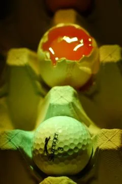 Open egg, behind a golf ball Stock Photos