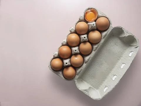 Open egg box with nine brown eggs and one broken egg showing yolk isolated... Stock Photos