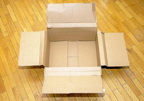 Open empty cardboard box package indoors on wooden floor interior Stock Photos
