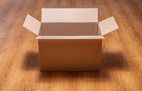 An open empty corrugated cardboard box sits on a brown wooden laminate floor. Stock Photos