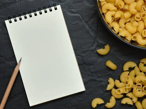 Open Empty Notebook and Pencil with Macaroni Pasta on Black Background Foto stock