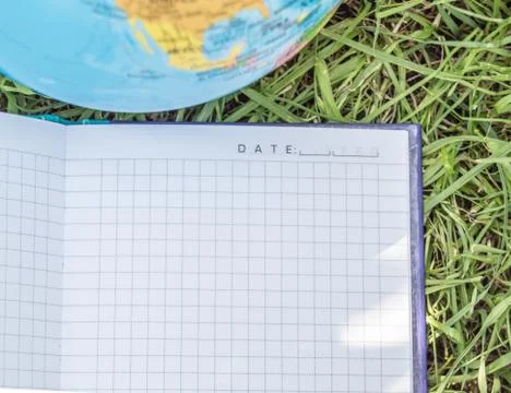 An open empty notebook lies on the grass near the globe, the concept of ecolo Stock Photos