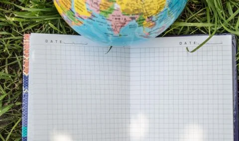An open empty notebook lies on the grass near the globe, the concept of ecolo Foto stock