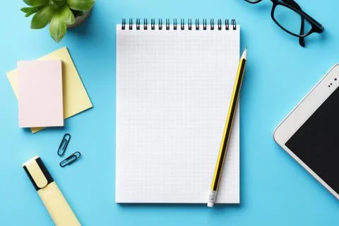 An open empty notepad, pen and tablet on a blue desk. Stock Photos