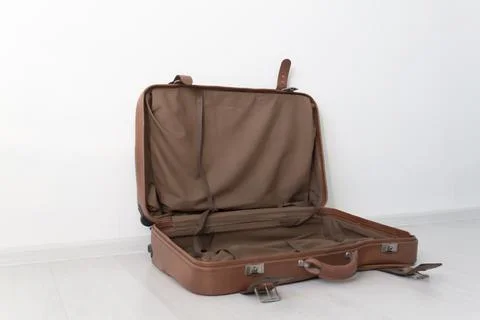 An open, empty, retro leather suitcase near a white wall. Stock Photos