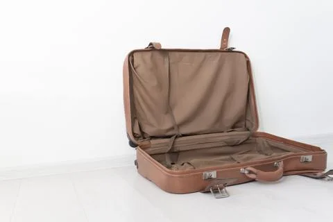 An open, empty, retro leather suitcase near a white wall. Stock Photos