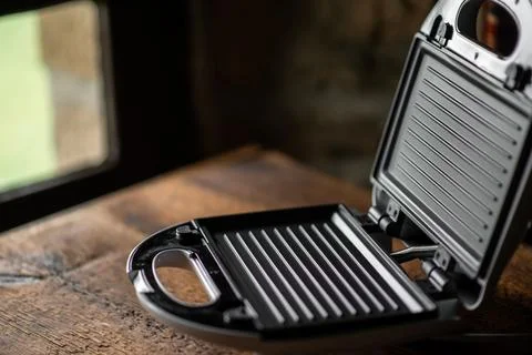 Open empty sandwich maker on the background of an old-fashioned house window. Stock Photos