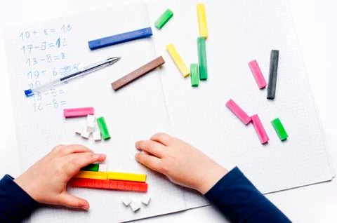 Open exercise book with colored plastic number rods on white background. Stock Photos