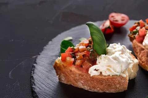 Open-faced bread toast with cheese and vegetables on black plate Stock Photos